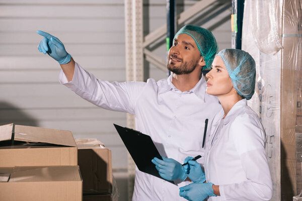 handsome storekeeper pointing with finger while looking away near attractive colleague