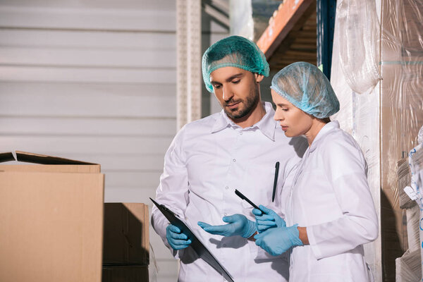 two storekeepers in white coats and hairnets looking at clipboard in warehouse
