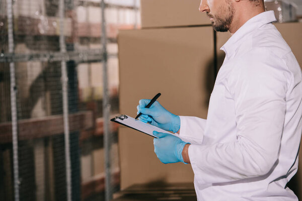 cropped view of storekeeper writing on clipboard near cardboard boxes