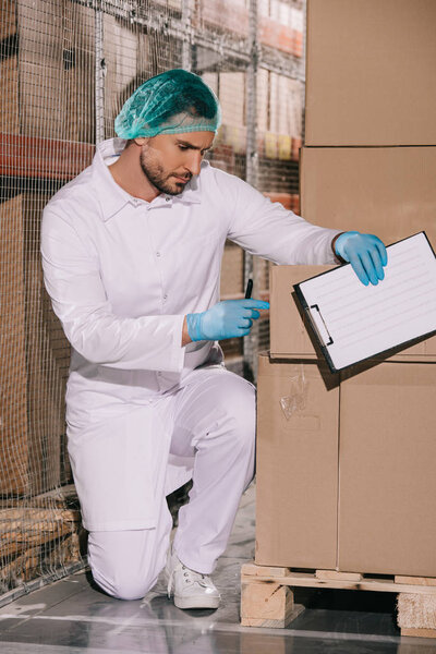 concentrated storekeeper inspecting cardboard box while holding clipboard