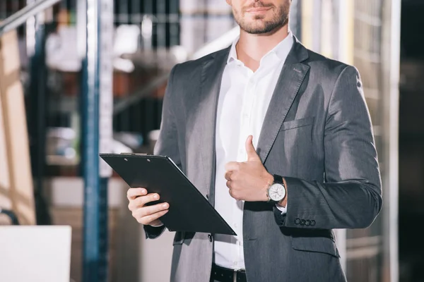 cropped view of businessman in formal wear holding clipboard in warehouse