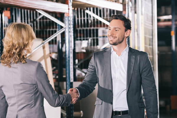 smiling businessman shaking hands with businesswoman in warehouse