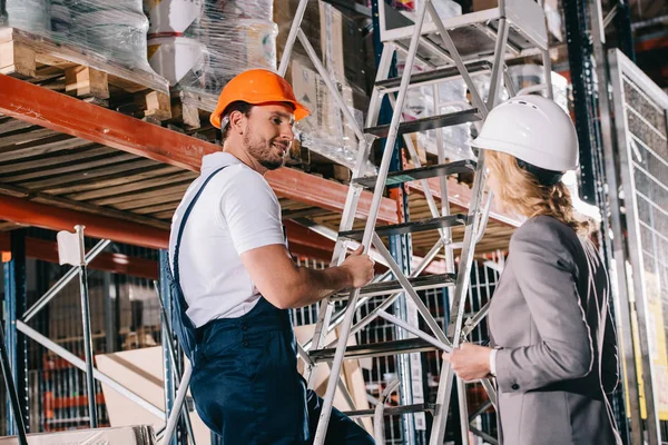 Trabajador Almacén Sonriente Pie Escalera Mirando Mujer Negocios Casco — Foto de Stock