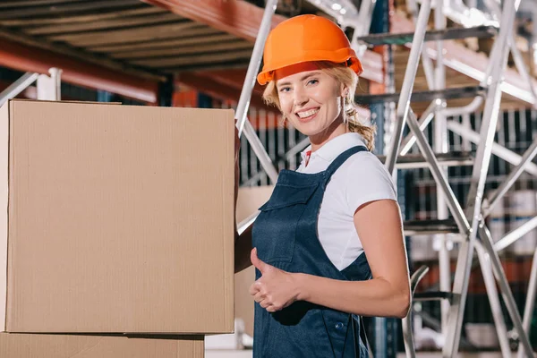 Smiling Workwoman Looking Camera Showing Thumb While Standing Cardboard Boxes — Stock Photo, Image