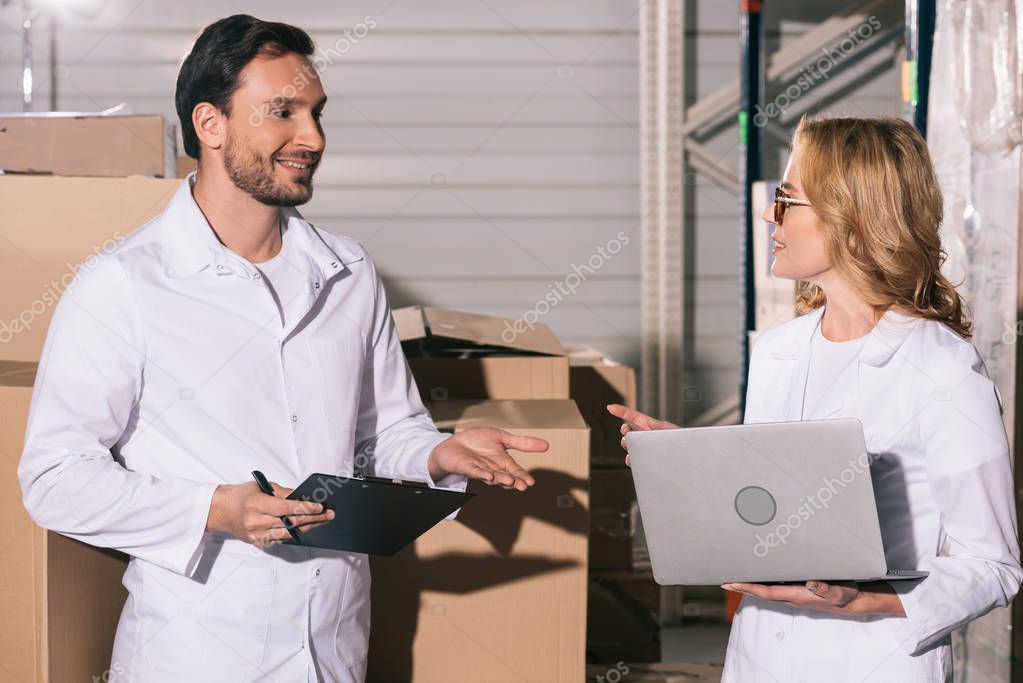 handsome storekeeper talking to colleague holding laptop in warehouse
