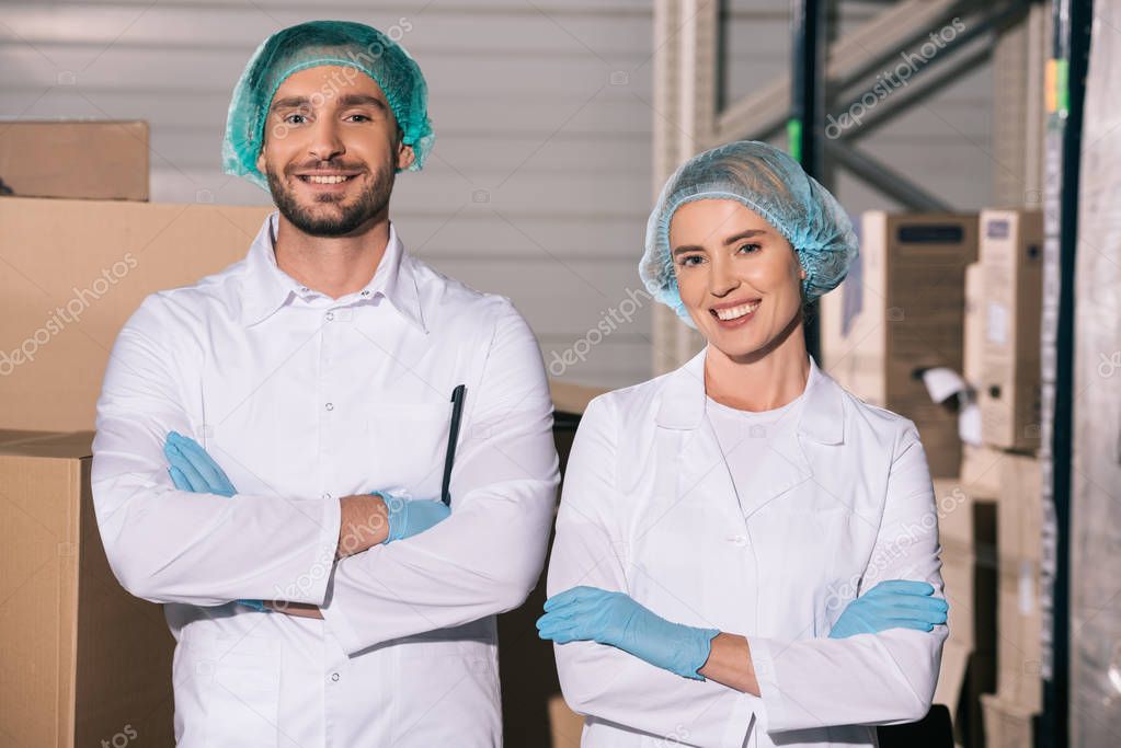 two cheerful storekeepers standing with crossed arms while smiling at camera