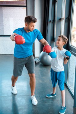 Baba boks eldiveni giymiş yakışıklı oğlana bakarken spor salonunda çalışıyor. 