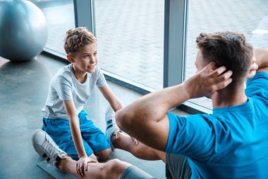 Tatlı çocuğun seçici odağı babasının spor paspası üzerinde egzersiz yapışına bakıyor. 