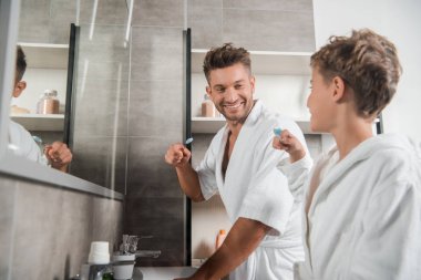selective focus of happy father looking at son with toothbrush  clipart