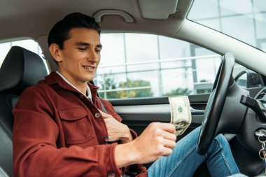 Taksi şoförü arabada dolar banknotu tutuyor.