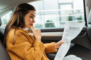 Taksinin arka koltuğunda gazete okuyan düşünceli genç bir kadın.
