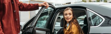 Taxi driver opening car door for smiling woman, panoramic shot clipart