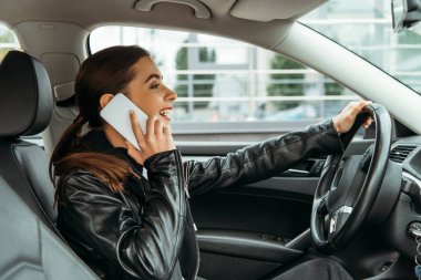 Gülümseyen kadın araba sürerken telefonla konuşuyor.