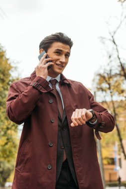 İş adamı akıllı telefondan konuşuyor ve caddedeki kol saatini kontrol ediyor.