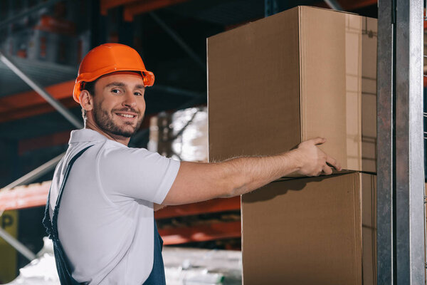 cheerful loader smiling at camera while holding cardboard box
