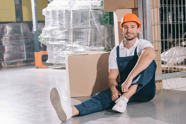 smiling loader sitting on floor near cardboard boxes and smiling at camera