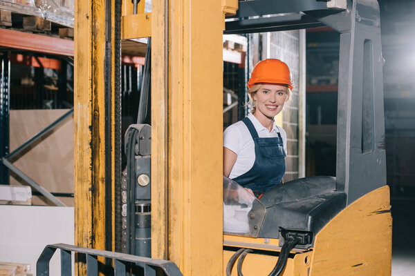 attractive workwoman sitting in forklift loader and smiling at camera