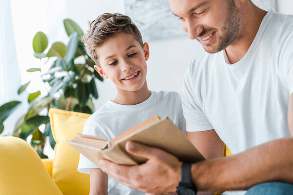 selective focus of happy father reading book near kid 