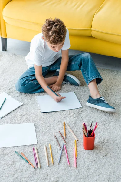 귀여운 아이가 노란색 카펫에 앉아서 집에서 종이에 그림을 그리는 — 스톡 사진