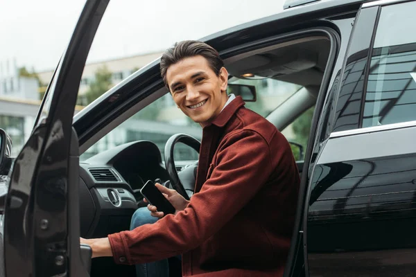 Усміхнений Таксист Сидить Машині Відкритими Дверима Тримає Смартфон — стокове фото