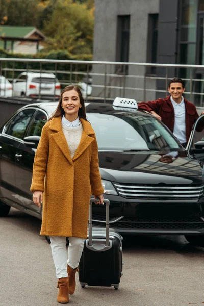 スーツケースと笑顔のタクシー運転手を背景に車で若い女性 — ストック写真