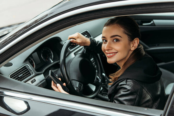 Smiling female taxi driver holding smartphone in car