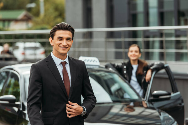 Selective focus of smiling businessman and taxi driver by car