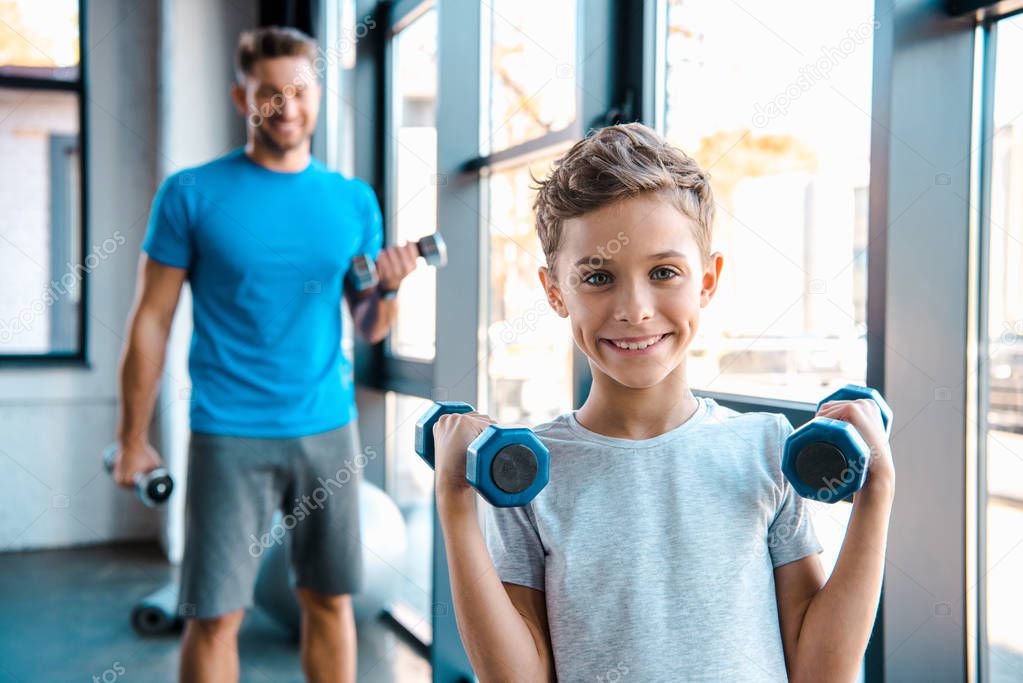 selective focus cute kid exercising with dumbbells near father 