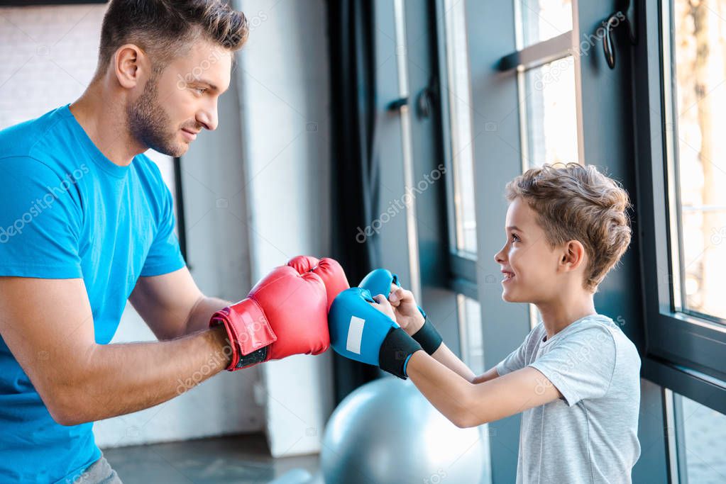 side view of handsome father in boxing gloves looking at cute son 