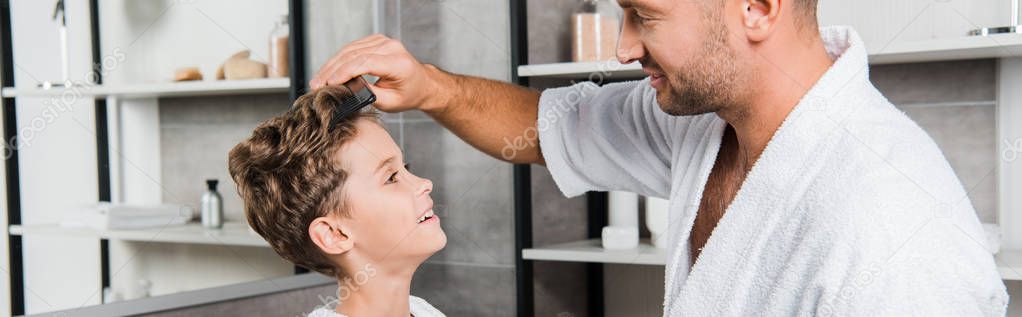 panoramic shot of handsome father brushing hair of cute son in bathroom 