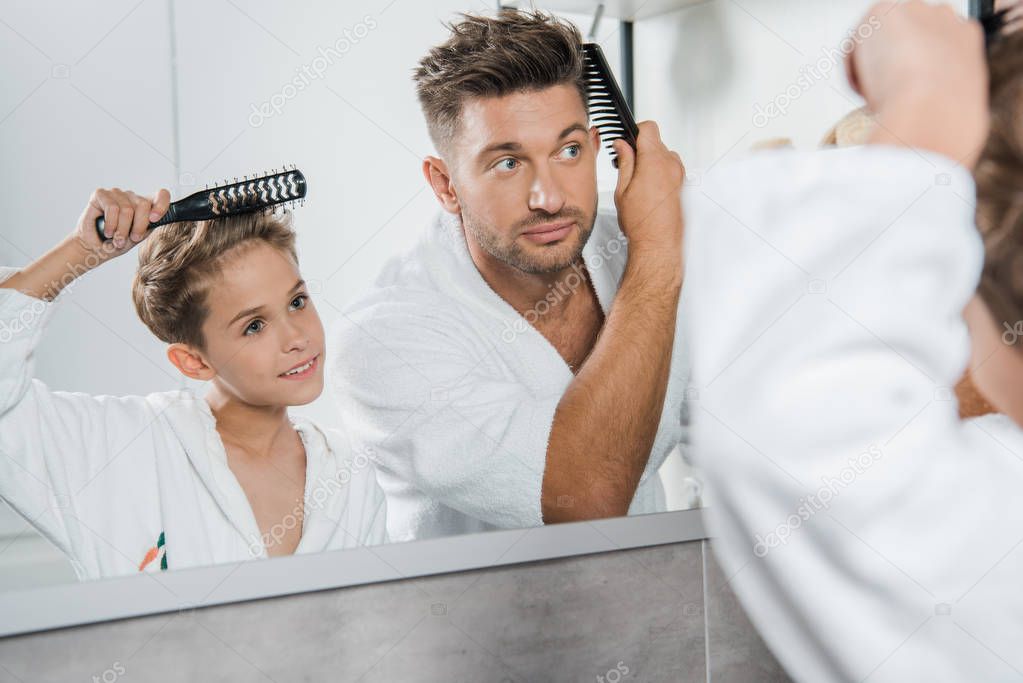selective focus of handsome man and cute kid brushing hair in bathroom 