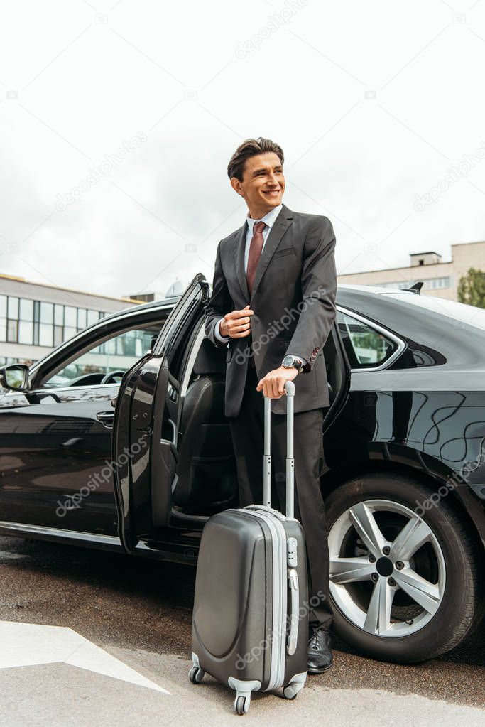 Smiling businessman with suitcase standing by taxi