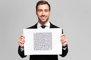 smiling and handsome businessman holding paper with labyrinth isolated on grey  clipart