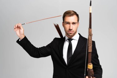 handsome businessman in suit holding bow and arrow isolated on grey  clipart