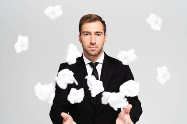 selective focus of businessman in suit throwing crumpled papers isolated on grey clipart