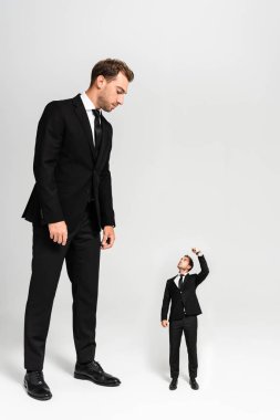 businessman in suit looking at marionette showing fist on grey background  clipart