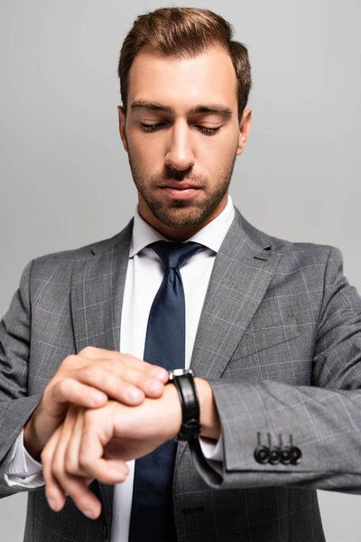 Красивый бизнесмен в костюме смотрит на наручные часы, изолированные на сером
 