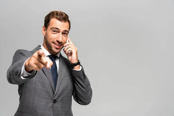 Handsome Smiling Businessman Suit Talking Smartphone Pointing Finger Isolated Grey — Stock Photo, Image