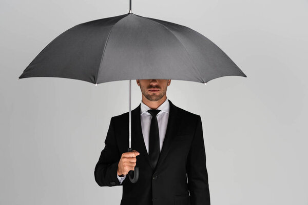 confident businessman in suit holding umbrella isolated on grey 