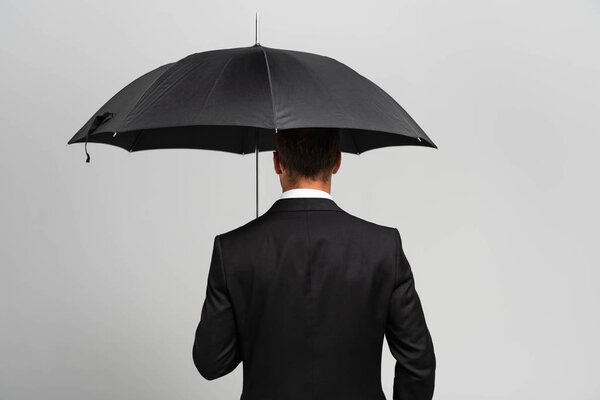 back view of businessman in suit holding umbrella isolated on grey 