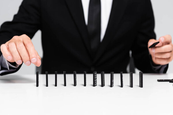 cropped view of businessman in suit picking domino from row isolated on grey 