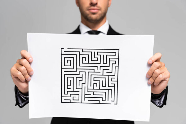 обрезанный взгляд бизнесмена, держащего бумагу с лабиринтом изолированной на сером
 