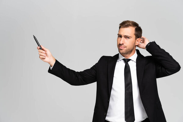pensive businessman in suit holding marker isolated on grey