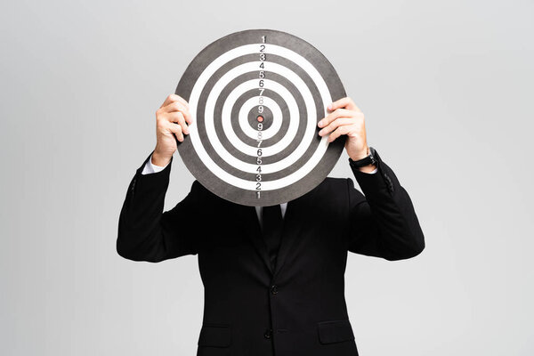 businessman in suit obscuring face with darts board isolated on grey