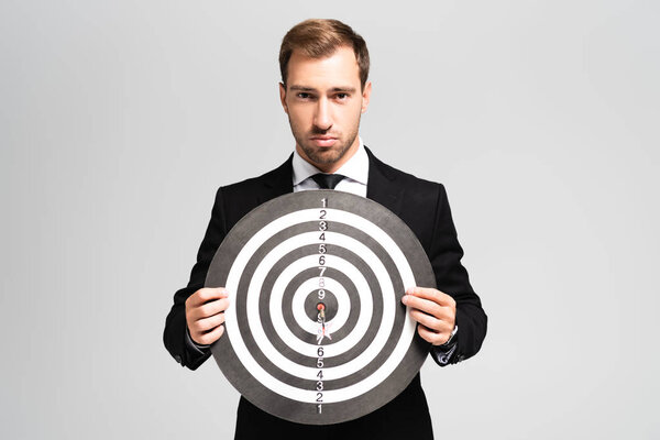 handsome businessman in suit holding darts board isolated on grey