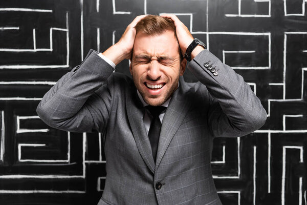 сердитый бизнесмен в костюме, стоящий возле лабиринта и трогательная голова
 