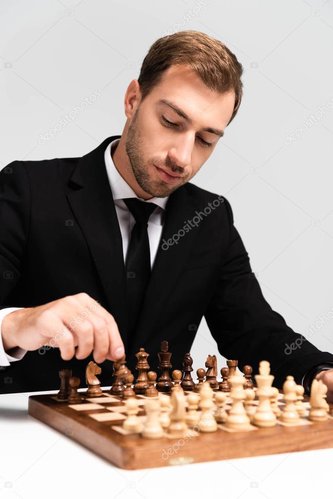 handsome businessman in suit playing chess isolated on grey 