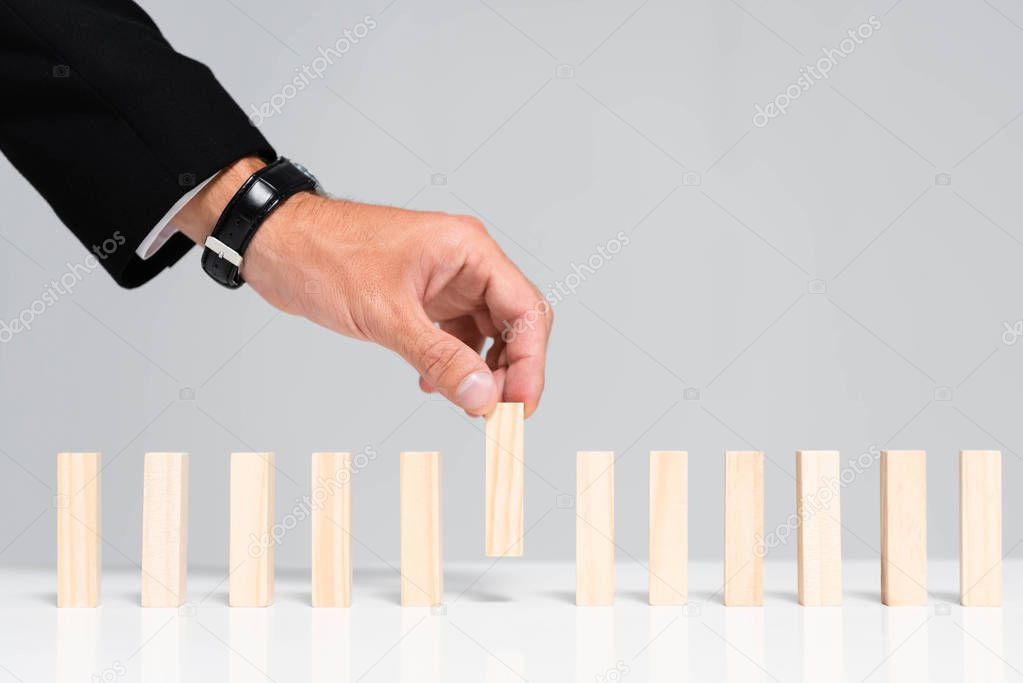 cropped view of man picking wooden block from row isolated on grey 