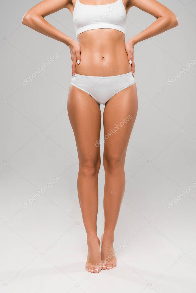 cropped view of beautiful slim woman in underwear posing on tiptoe on grey background