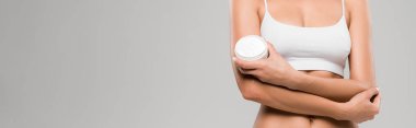 cropped view of woman in underwear holding cosmetic cream isolated on grey, panoramic shot
